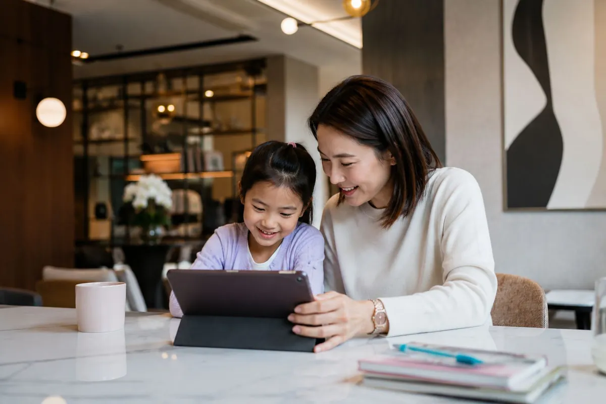 A mother and daughter smiling together while looking at a tablet at home